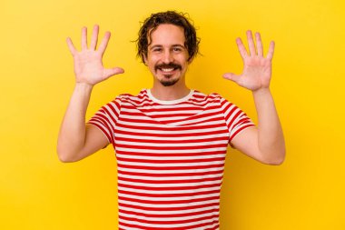 Sarı arka planda izole edilmiş genç beyaz adam on numarayı elleriyle gösteriyor..