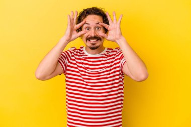 Sarı arka planda izole edilmiş genç beyaz adam bir başarı fırsatı bulmak için gözlerini açık tutuyor..