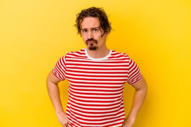 Sarı arka planda izole edilmiş genç beyaz adam yanakları patlatır, yorgun bir ifadeye sahiptir. Yüz ifadesi kavramı.