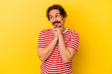 Sarı arka planda izole edilmiş genç beyaz adam ellerini çenesinin altında tutuyor ve mutlu bir şekilde yan tarafa bakıyor..