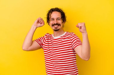 Sarı arka planda izole edilmiş genç beyaz adam özel bir günü kutluyor, atlıyor ve enerjiyle kollarını kaldırıyor..