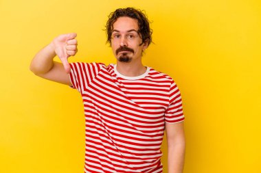 Sarı arka planda izole edilmiş genç beyaz adam baş parmağını aşağı gösteriyor, hayal kırıklığı konsepti..