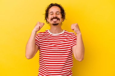 Sarı arka planda izole edilmiş genç beyaz adam zaferi, tutkuyu ve coşkuyu kutluyor, mutlu bir ifade..