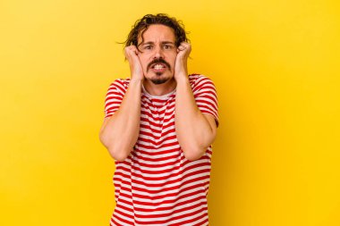 Kafkasyalı genç adam sarı arka planda izole edilmiş, ağlıyor, bir şeyden memnun değil, acı ve kafa karışıklığı kavramı..