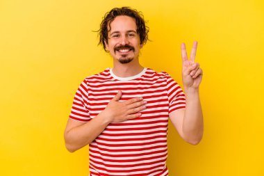 Sarı arka planda izole edilmiş genç beyaz adam yemin ediyor, elini göğsüne koyuyor..