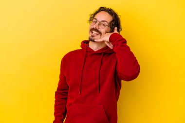 Sarı arka planda izole edilmiş genç beyaz adam parmaklarıyla bir cep telefonu hareketi gösteriyor..