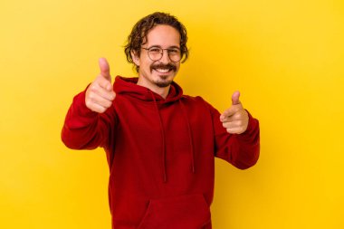Sarı arka planda izole edilmiş genç beyaz adam parmaklarıyla ön tarafı işaret ediyor..