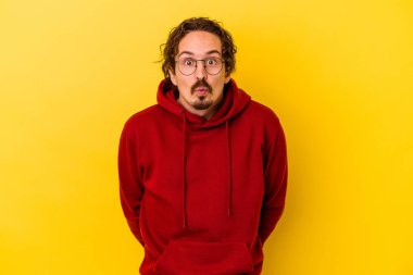 Sarı arka planda izole edilmiş genç beyaz adam omuzlarını silkeliyor ve gözleri açık..