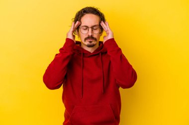 Sarı arka planda izole edilmiş genç beyaz adam tapınaklara dokunuyor ve baş ağrısı çekiyor..