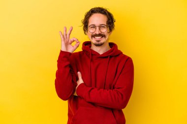 Sarı arka planda izole edilmiş genç beyaz bir adam bir göz kırptı ve elleriyle iyi bir jest yaptı..