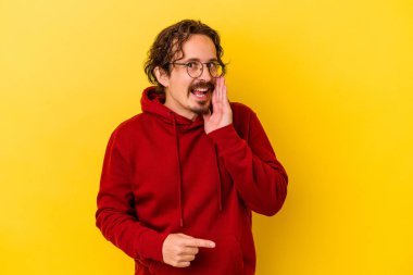 Sarı arka planda izole edilmiş genç beyaz bir adam bir dedikodu söylüyor, bir haber sunuyor..