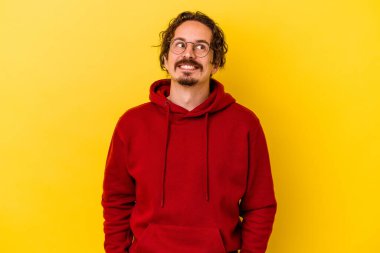 Sarı arka planda izole edilmiş genç beyaz adam gevşemiş ve mutlu gülüyor, boynunda dişlerini gösteriyor..