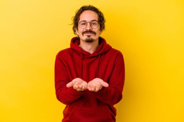 Sarı arka planda izole edilmiş genç beyaz bir adam elinde avuç içi bir şeyle kameraya sunuyor..