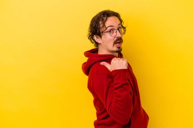 Kafkasyalı genç adam sarı arka planda izole edilmiş, başparmak uzakta, gülüyor ve kaygısız..