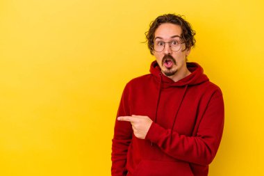 Sarı arka planda izole edilmiş genç beyaz adam gülümsüyor ve boş alanda bir şeyler gösteriyor..