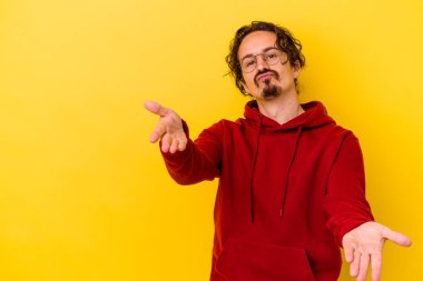 Sarı arka planda izole edilmiş genç, beyaz bir adam. Dudaklarını kıvırıyor, avuç içlerini tutuyor ve hava öpücüğü yolluyor..