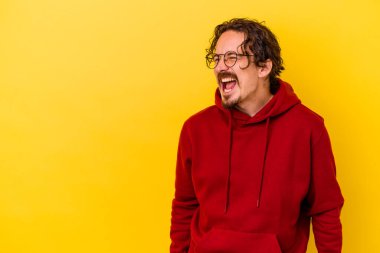 Sarı arka planda izole edilmiş genç beyaz bir adam çok kızgın, öfkeli, hayal kırıklığına uğramış diye bağırıyor..