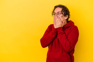 Kafkasyalı genç adam sarı arka planda izole edilmiş. Düşünceli bir şekilde, ağzını eliyle kapatan bir fotokopi odasına bakıyor..