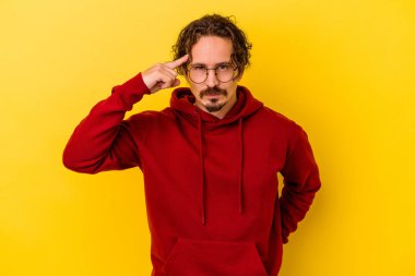 Sarı arka planda izole edilmiş genç beyaz bir adam şakağı parmağıyla işaret ediyor, düşünüyor ve bir göreve odaklanıyor..