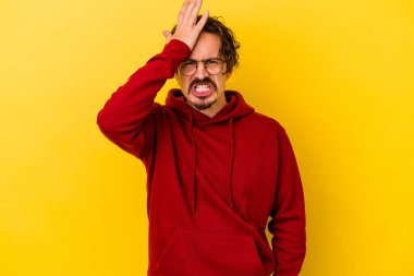 Sarı arka planda izole edilmiş genç beyaz bir adam bir şeyi unutuyor. Alnına avuç içi ve gözlerini kapayarak vuruyor..