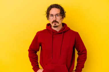 Sarı arka planda izole edilmiş genç beyaz adam şaşkın, şüpheli ve güvensiz hissediyor..