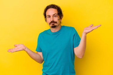 Kafkasyalı genç adam sarı arka planda izole edilmiş. Kafası karışmış ve omuz silkiyor. Kopya alanını tutmak için..