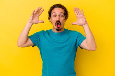 Sarı arka planda izole edilmiş genç beyaz bir adam zaferi ya da başarıyı kutluyor, şaşırıyor ve şok oluyor..