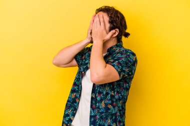 Sarı arka planda izole edilmiş genç beyaz adam elleriyle gözlerini kapatmaktan korkuyor..