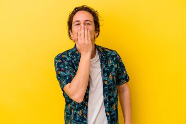 Sarı arka planda izole edilmiş genç beyaz adam şok olmuş, ağzı ellerle kaplanmış, yeni bir şey keşfetmeye hevesli..