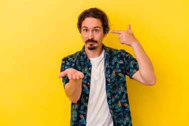 Genç beyaz adam sarı arka planda izole edilmiş ve elinde bir ürün var..