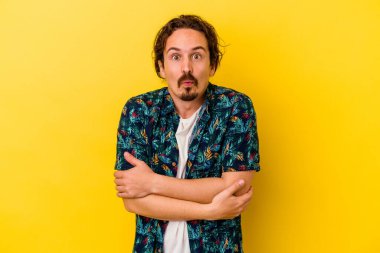 Sarı arka planda izole edilmiş genç beyaz adam omuzlarını silkeliyor ve gözleri açık..