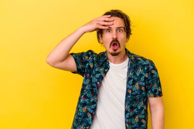 Kafkasyalı genç adam sarı arka planda izole edilmiş, uzaklara bakıyor ve elini alnına koyuyor..
