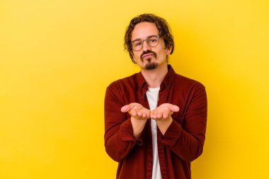 Sarı arka planda izole edilmiş genç, beyaz bir adam. Dudaklarını kıvırıyor, avuç içlerini tutuyor ve hava öpücüğü yolluyor..