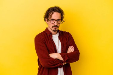 Sarı arka planda izole edilmiş genç beyaz adam hoşnutsuzca kaşlarını çatmış, kollarını kavuşturmuş..