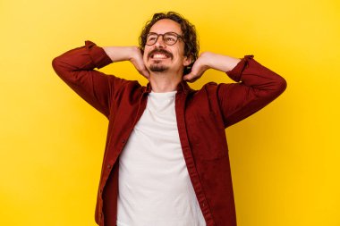 Sarı arka planda izole edilmiş genç beyaz bir adam kendini güvende hissediyor, elleri başının arkasında..