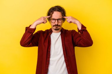 Sarı arka planda izole edilmiş genç beyaz adam bir göreve odaklanmış, işaret parmaklarını işaret ediyor..