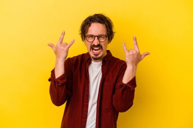 Sarı arka planda izole edilmiş genç beyaz adam boynuzlarını devrim konsepti olarak gösteriyor..