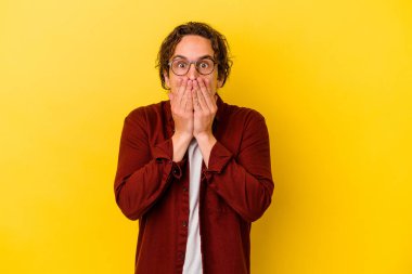 Sarı arka planda izole edilmiş genç beyaz adam elleriyle ağzını kapatırken şok oldu..