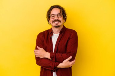 Sarı arka planda izole edilmiş genç beyaz adam kendini güvende hissediyor, kararlılıkla kollarını kavuşturuyor..