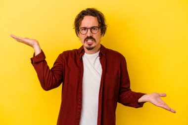 Kafkasyalı genç adam sarı arka planda izole edilmiş. Kafası karışmış ve omuz silkiyor. Kopya alanını tutmak için..