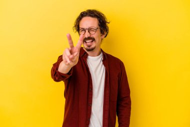 Sarı arka planda izole edilmiş genç beyaz adam iki numarayı parmaklarıyla gösteriyor..