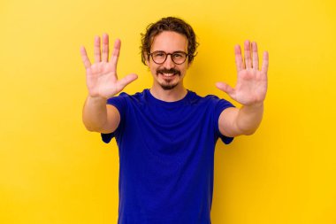 Sarı arka planda izole edilmiş genç beyaz adam on numarayı elleriyle gösteriyor..