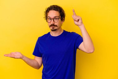 Genç beyaz adam sarı arka planda izole edilmiş ve elinde bir ürün var..