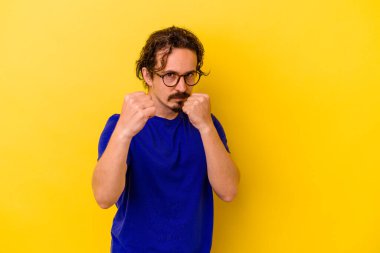 Sarı arka planda izole edilmiş genç beyaz bir adam bir tartışma yüzünden yumruk atıyor, öfkeleniyor, kavga ediyor, boks yapıyor.