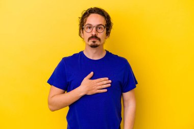 Sarı arka planda izole edilmiş genç beyaz adam yemin ediyor, elini göğsüne koyuyor..