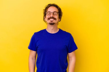 Sarı arka planda izole edilmiş genç beyaz adam gülüyor ve gözlerini kapıyor, rahatlamış ve mutlu hissediyor..