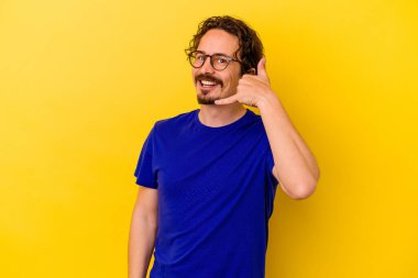 Sarı arka planda izole edilmiş genç beyaz adam parmaklarıyla bir cep telefonu hareketi gösteriyor..