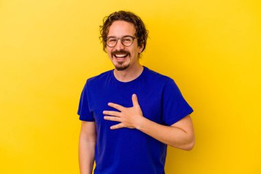 Sarı arka planda izole edilmiş genç beyaz adam yüksek sesle gülüyor ve elini göğsüne koyuyor..