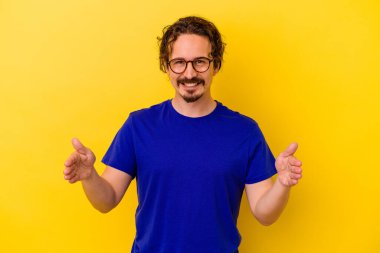 Sarı arka planda izole edilmiş genç beyaz adam iki eliyle bir şey tutuyor, ürün sunumu..