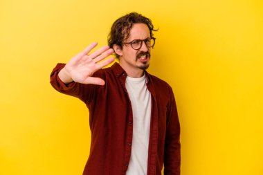 Sarı arka planda izole edilmiş genç beyaz adam tiksinti belirtisi gösteren birini reddediyor..